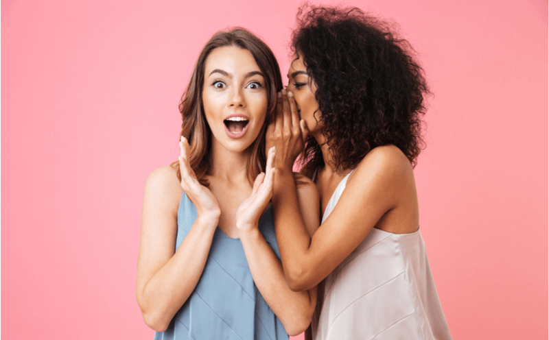 one girl whispering in another girl's ear